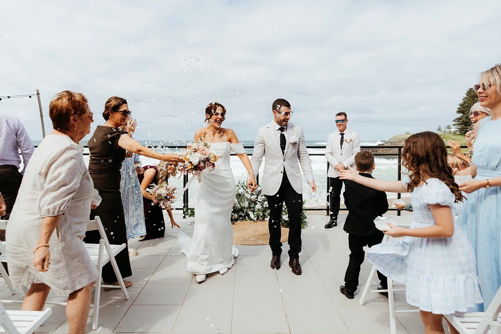 Guests throwing petals as the couple walk out of a seaside ceremony