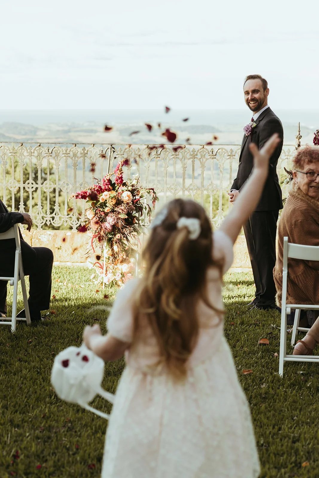 A flower girl throwing petals down the aisle at a garden ceremony by the sea